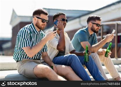 leisure, technology and people concept - happy male friends with smartphones drinking beer on street in summer. men with smartphones drinking beer on street
