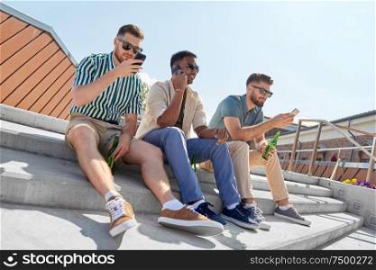leisure, technology and people concept - happy male friends with smartphones drinking beer and talking on street in summer. men with smartphones drinking beer on street