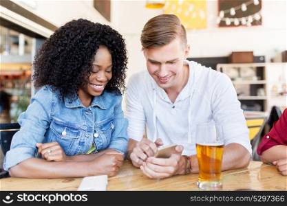leisure, technology and people concept - happy man and woman with smartphone and beer at bar or restaurant. happy man and woman with smartphone at bar