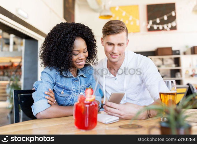 leisure, technology and people concept - happy man and woman with smartphone and beer at bar or restaurant. happy man and woman with smartphone at bar