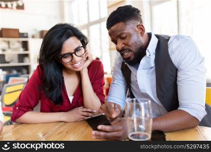 leisure, technology and people concept - happy man and woman with smartphones and drinks at bar or restaurant. happy man and woman with smartphones at bar