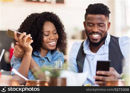 leisure, technology and people concept - happy man and woman with smartphones eating at restaurant. happy man and woman with smartphones at restaurant