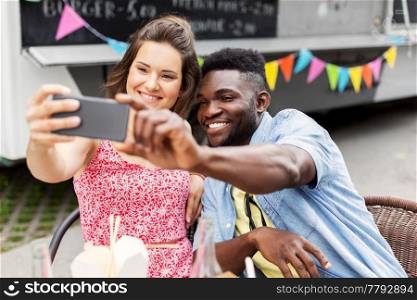leisure, technology and people concept - happy mixed race couple taking selfie by smartphone at food truck. mixed race couple taking selfie at food truck
