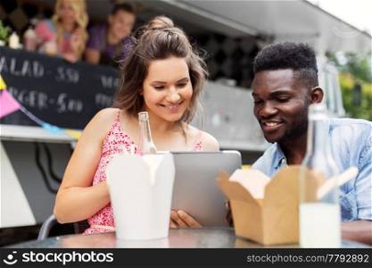 leisure, technology and people concept - happy mixed race couple with tablet pc computer eating at food truck. mixed race couple with tablet pc at food truck