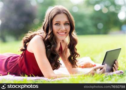leisure, technology and people concept - happy smiling woman with tablet computer lying on picnic blanket at summer park. happy woman with tablet computer on picnic at park