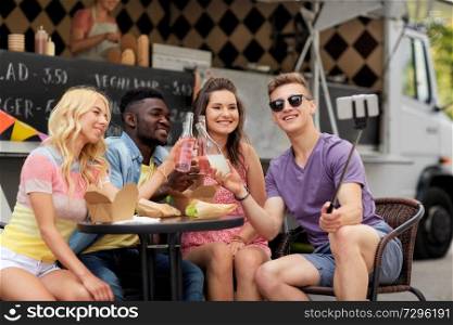 leisure, technology and people concept - happy young friends with food and drinks and taking selfie at food truck. happy young friends taking selfie at food truck