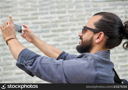 leisure, technology and people concept - hipster man taking picture or video by smartphone on street