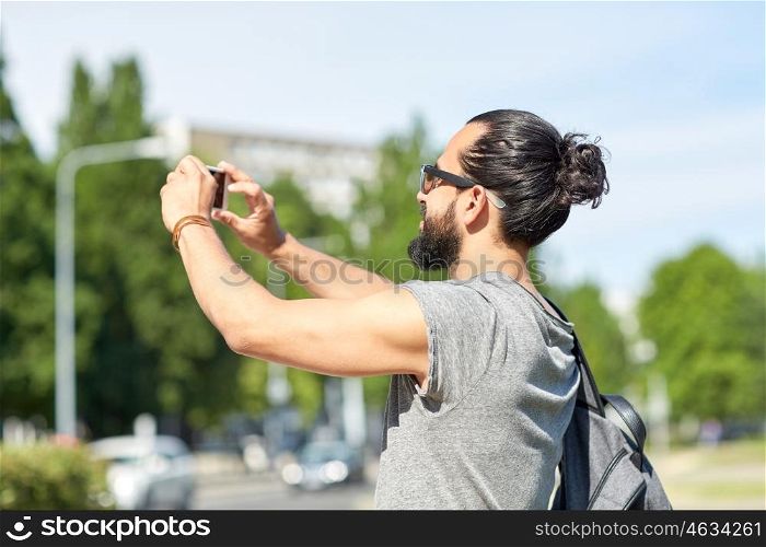 leisure, technology and people concept - hipster man taking picture or video by smartphone on street