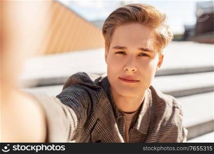 leisure, technology and people concept - nice young man or teenage boy taking selfie in city. young man or teenage boy taking selfie in city
