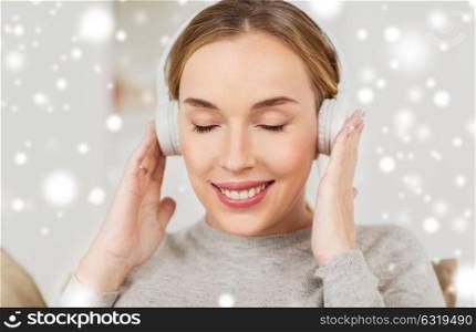 leisure, technology and people concept - smiling woman with headphones listening to music at home over snow. woman with headphones listening to music at home