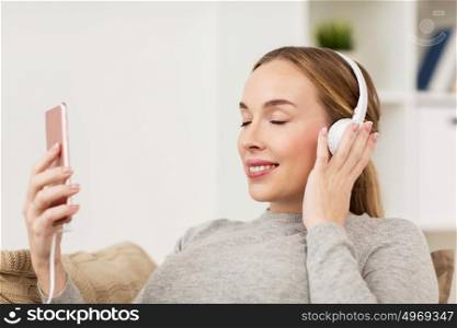 leisure, technology and people concept - smiling woman with smartphone and headphones listening to music at home. woman with smartphone and headphones at home