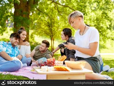 leisure, technology and people concept - woman using smartphone at picnic with friends in summer park. woman using smartphone at picnic with friends