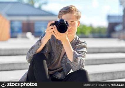 leisure, technology and people concept - young man or teenage boy with digital camera photographing in city. young man with camera photographing in city