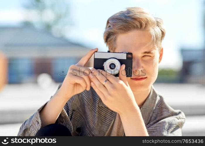 leisure, technology and people concept - young man or teenage boy with camera photographing in city. young man with camera photographing in city