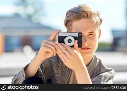 leisure, technology and people concept - young man or teenage boy with camera photographing in city. young man with camera photographing in city
