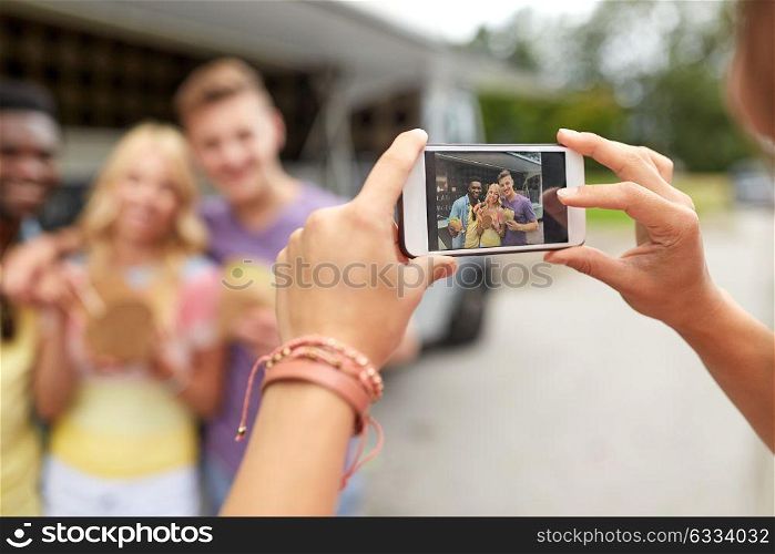 leisure, technology and people concept - young woman taking picture of her happy friends eating hamburgers and wok at food truck. woman photographing friends eating at food truck