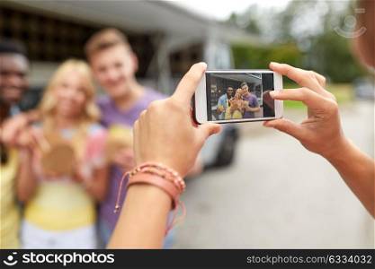 leisure, technology and people concept - young woman taking picture of her happy friends eating hamburgers and wok at food truck. woman photographing friends eating at food truck