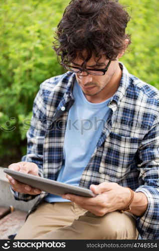 leisure, technology, communication and people concept - close up of creative man in glasses with tablet pc computer sitting on bench outdoors
