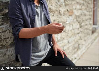 leisure, technology, communication and people concept - close up of man with smartphone at stone wall on street
