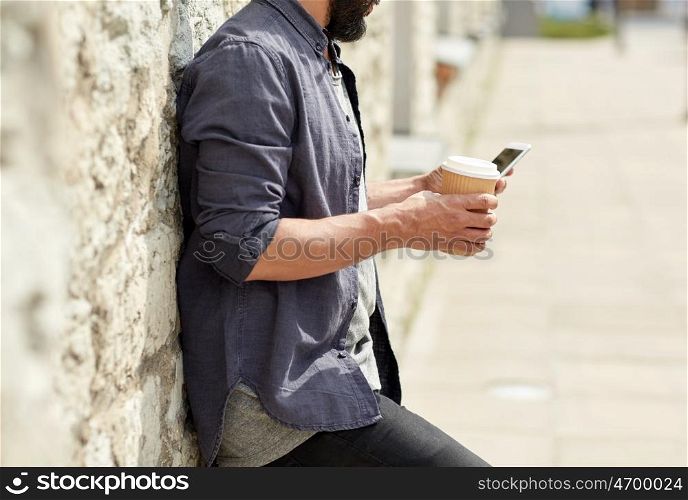 leisure, technology, communication and people concept - close up of man with smartphone drinking coffee from disposable paper cup on city street