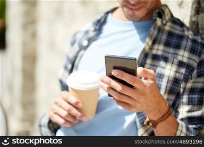 leisure, technology, communication and people concept - close up of man with smartphone and coffee cup texting message on city street
