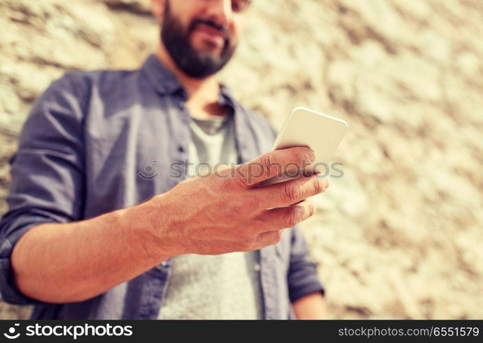 leisure, technology, communication and people concept - close up of man with smartphone at stone wall on street. close up of man with smartphone at stone wall. close up of man with smartphone at stone wall