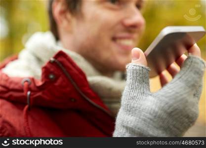 leisure, technology, communication and people concept - close up of smiling hipster man using voice command recorder or calling on smartphone in autumn