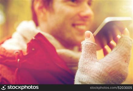 leisure, technology, communication and people concept - close up of smiling hipster man using voice command recorder or calling on smartphone in autumn. close up of man recording voice on smartphone