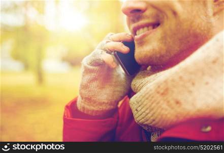 leisure, technology, communication and people concept - close up of smiling young man calling on smartphone in autumn. close up of man with smartphone calling in autumn