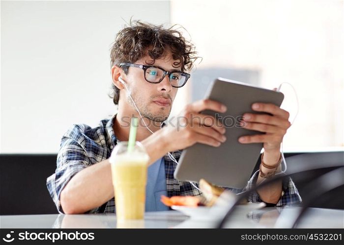 leisure, technology, communication and people concept - creative man with tablet pc computer and earphones listening to music at cafe table
