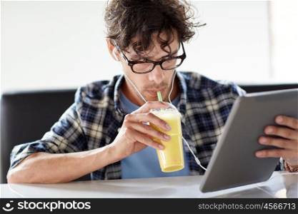leisure, technology, communication and people concept - creative man with tablet pc computer and earphones listening to music and drinking shake at cafe table