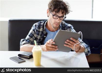 leisure, technology, communication and people concept - creative man with tablet pc computer and earphones listening to music at cafe table