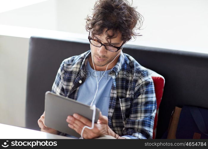 leisure, technology, communication and people concept - creative man with tablet pc computer and earphones listening to music at cafe table