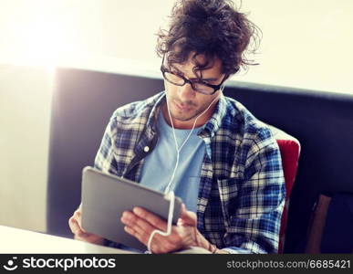leisure, technology, communication and people concept - creative man with tablet pc computer and earphones listening to music at cafe table. man with tablet pc and earphones sitting at cafe