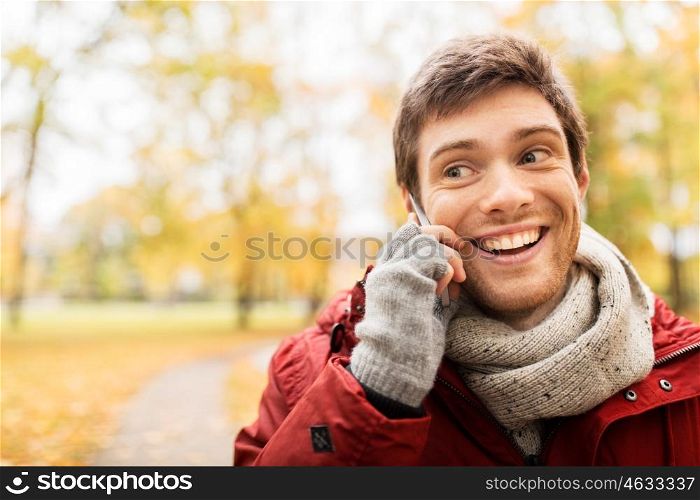 leisure, technology, communication and people concept - happy smiling young man calling on smartphone at autumn park