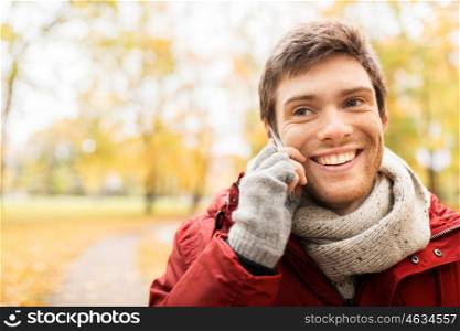 leisure, technology, communication and people concept - happy smiling young man calling on smartphone at autumn park