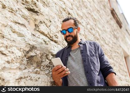 leisure, technology, communication and people concept - man in sunglasses texting message on smartphone at stone wall