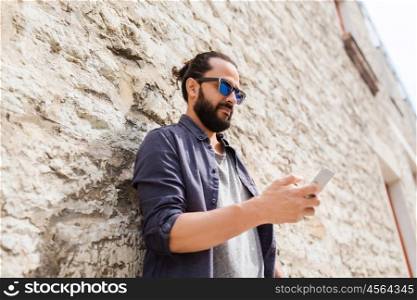 leisure, technology, communication and people concept - man in sunglasses texting message on smartphone at stone wall