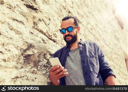 leisure, technology, communication and people concept - man in sunglasses texting message on smartphone at stone wall. man texting message on smartphone at stone wall. man texting message on smartphone at stone wall