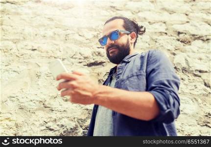 leisure, technology, communication and people concept - man in sunglasses texting message on smartphone at stone wall. man texting message on smartphone at stone wall. man texting message on smartphone at stone wall