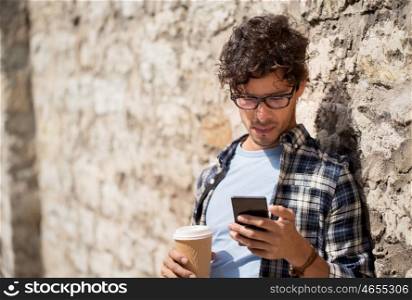 leisure, technology, communication and people concept - man with smartphone drinking coffee from disposable paper cup and texting message on city street. man with smartphone drinking coffee on city street