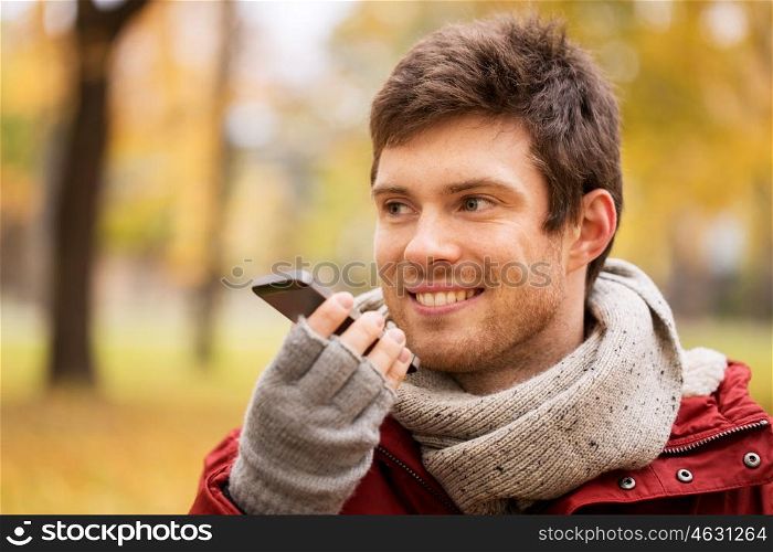 leisure, technology, communication and people concept - smiling hipster man using voice command recorder or calling on smartphone at autumn park