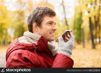 leisure, technology, communication and people concept - smiling hipster man using voice command recorder or calling on smartphone at autumn park
