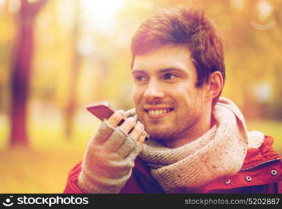 leisure, technology, communication and people concept - smiling hipster man using voice command recorder or calling on smartphone at autumn park. man recording voice on smartphone at autumn park