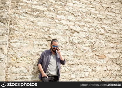 leisure, technology, communication and people concept - smiling man calling on smartphone at stone wall on city street