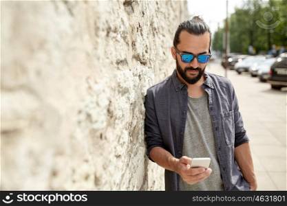 leisure, technology, communication and people concept - smiling man texting message on smartphone at stone wall on city street