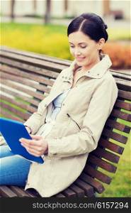 leisure, technology, communication and people concept - smiling woman with tablet pc computer sitting on bench in park