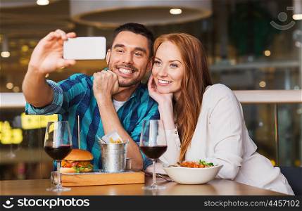 leisure, technology, date, people and holidays concept - happy couple having dinner and taking selfie by smartphone at restaurant