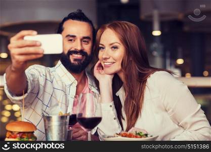 leisure, technology, date, people and holidays concept - happy couple having dinner and taking selfie by smartphone at restaurant. couple taking selfie by smartphone at restaurant
