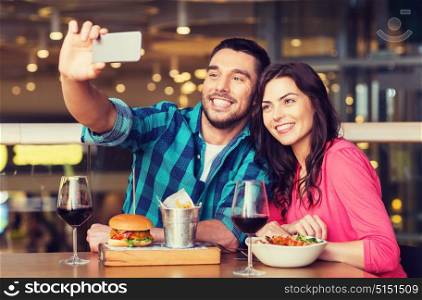leisure, technology, date, people and holidays concept - happy couple having dinner and taking selfie by smartphone at restaurant. couple taking selfie by smartphone at restaurant